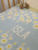 A knitted blanket with a floral pattern featuring daisies, in blue, white, and yellow colours, with the name 'ISLA' knitted into it. Knitted on the Mornington Peninsula in Victoria Australia. The Original Name Blanket from The Knit Studio