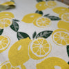 Close-up of a knitted blanket with a citrus fruit pattern, predominantly yellow with green leaves. Organic Cotton