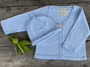 A blue fine knit cardigan and a matching beanie hat for babies, laid flat on a wooden surface. Knitted in Organic Cotton, Knitted to order means sustainable fashion.