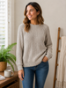 Woman wearing a fawn merino wool jumper and blue jeans.